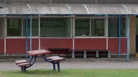 Une table de pique-nique déséquilibrée sur un patch de gazon devant un des bâtiments de Patchway Community School.