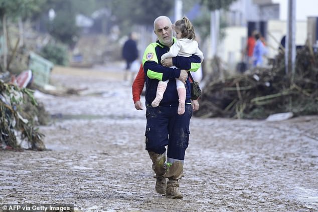 Un membre de la Protection Civile porte un enfant dans une rue inondée.