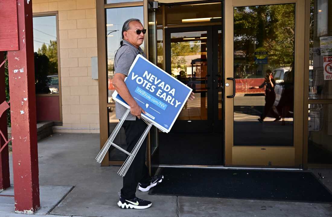 Little Buck Harjo portant des panneaux 'Nevada Votes Early' lors d'un événement à Reno, Nevada, le 15 octobre 2024.