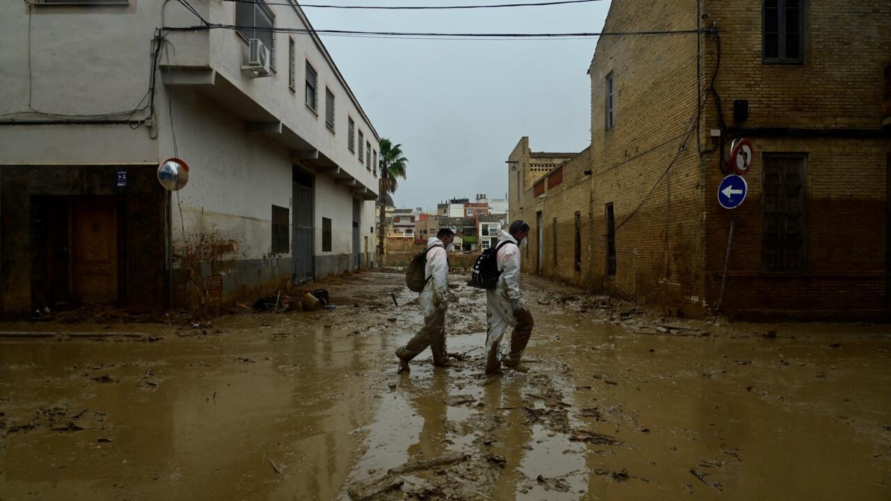 Des hommes en combinaisons de protection marchent dans une rue couverte de boue à Paiporta, au sud de Valence, Espagne.