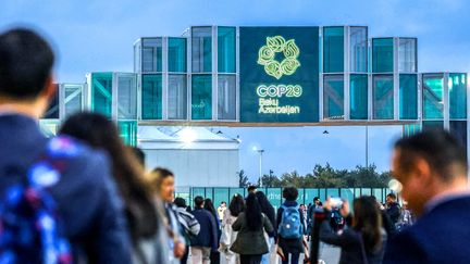 Des participants passent devant l'entrée de la COP29, un événement organisé par la CCNUCC au stade olympique de Bakou.