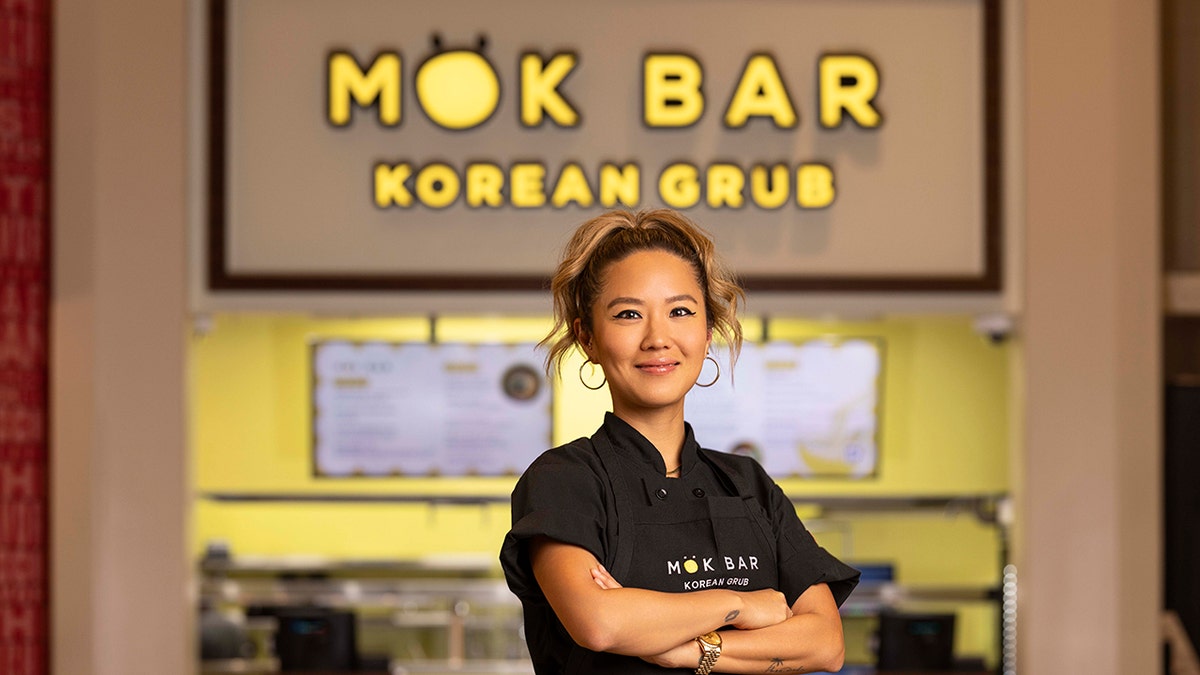 Chef Esther Choi posant avec des baguettes devant des bols de nourriture.