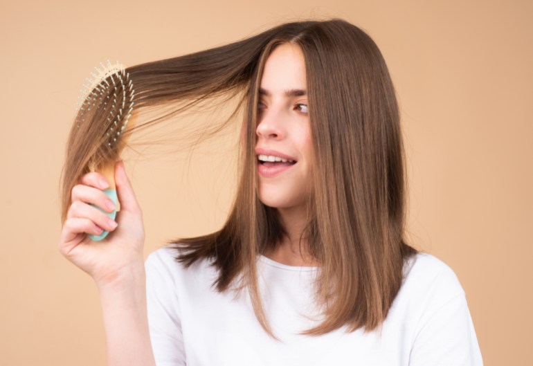 Portrait d'une belle femme brune peignant ses cheveux avec une brosse, isolée.