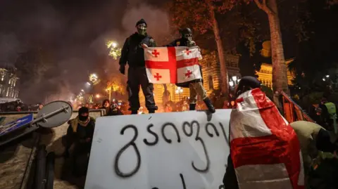 Un manifestant portant un drapeau géorgien se tient sur une barricade lors d'un affrontement avec la police le 1er décembre 2024.