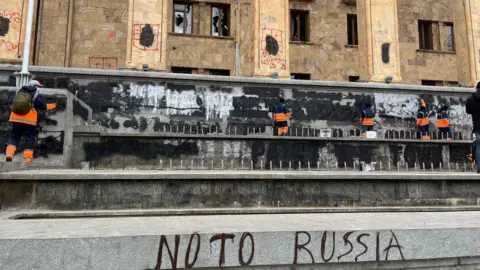 Des nettoyeurs effacent des graffitis sur les murs devant le parlement en Géorgie.